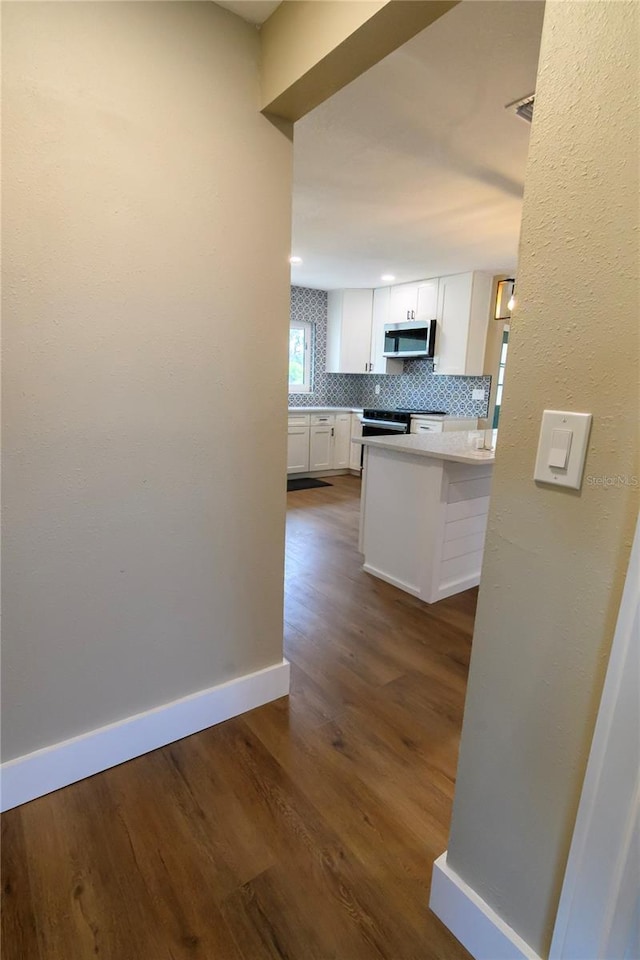 kitchen with backsplash, baseboards, stainless steel microwave, dark wood-style floors, and white cabinetry