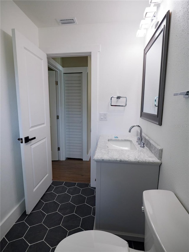 half bath with vanity, toilet, tile patterned floors, baseboards, and visible vents