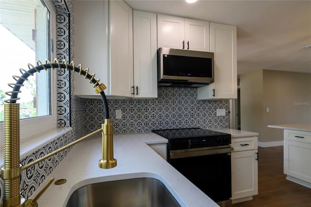 kitchen featuring stainless steel microwave, black range with electric cooktop, backsplash, and white cabinets