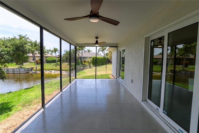 unfurnished sunroom featuring a water view, tile patterned floors, a wall of windows, and ceiling fan