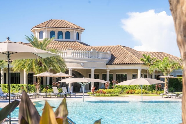 rear view of property with a community pool, stucco siding, a balcony, and a tile roof