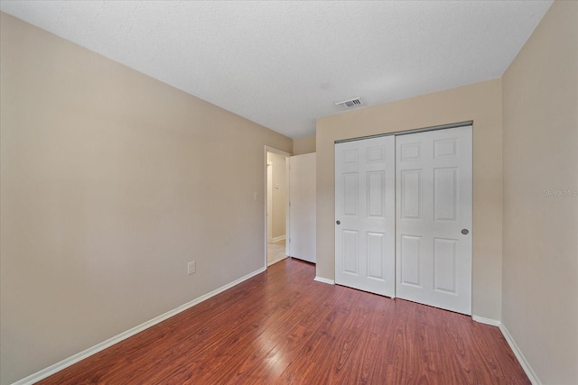unfurnished bedroom featuring baseboards, a closet, wood finished floors, and visible vents
