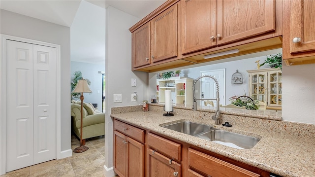 kitchen featuring light tile patterned flooring, brown cabinetry, light stone countertops, and a sink