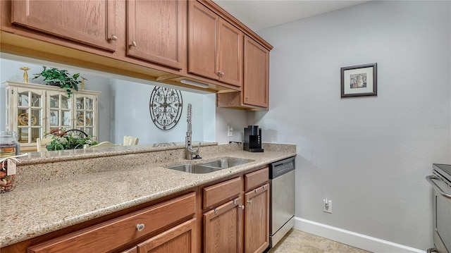 kitchen with baseboards, brown cabinetry, light stone counters, a sink, and stainless steel appliances