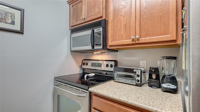 kitchen featuring light stone countertops, black microwave, stainless steel electric range oven, and a toaster
