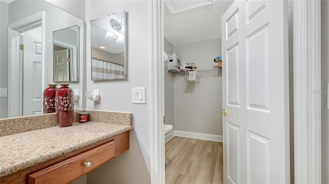 full bathroom with toilet, wood finished floors, vanity, a spacious closet, and baseboards