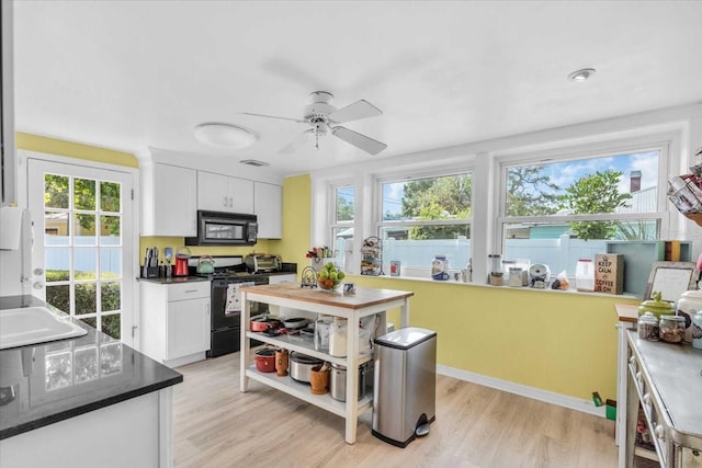 5012 Eastchester Dr, Sarasota, FL 34234 - kitchen with black microwave, gas stove, light wood finished floors, white cabinetry, and a wealth of natural light