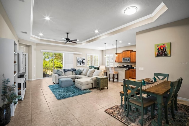 living area with light tile patterned floors, a tray ceiling, visible vents, and ceiling fan