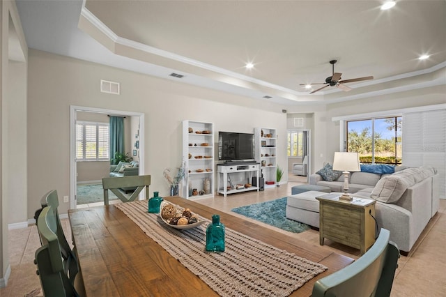 living room with visible vents, a ceiling fan, a tray ceiling, and ornamental molding