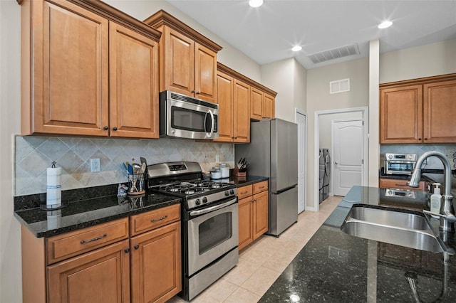 kitchen with appliances with stainless steel finishes, a sink, visible vents, and dark stone countertops