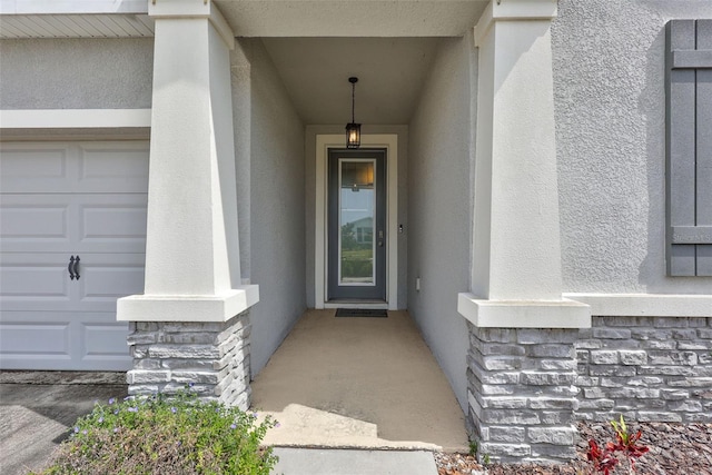 entrance to property featuring a garage, stucco siding, and stone siding