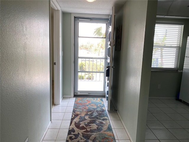doorway with a textured wall, light tile patterned floors, baseboards, and a textured ceiling