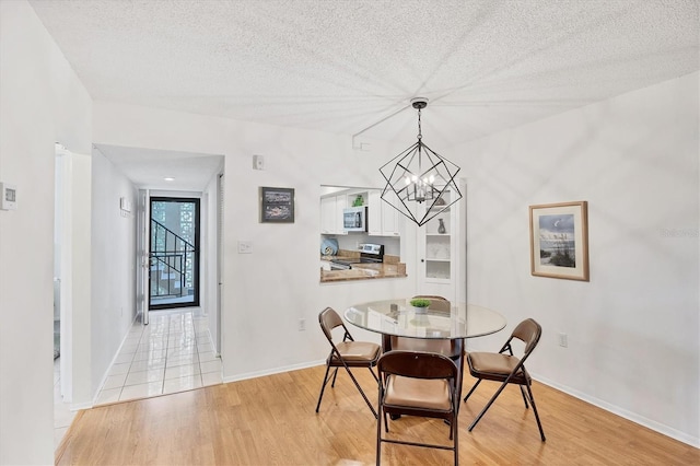 2280 Stickney Point Rd Unit 420, Sarasota, FL 34231 - dining area featuring an inviting chandelier, baseboards, light wood finished floors, and a textured ceiling