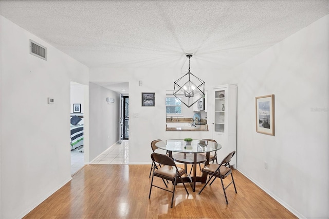 2280 Stickney Point Rd Unit 420, Sarasota, FL 34231 - dining room with a textured ceiling, visible vents, light wood-type flooring, baseboards, and a chandelier