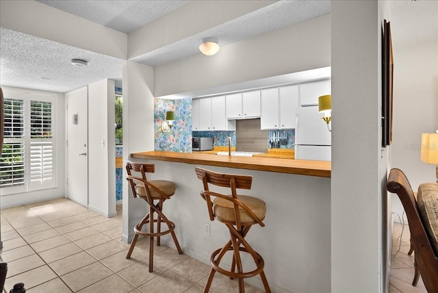 kitchen with freestanding refrigerator, a textured ceiling, a breakfast bar, light tile patterned flooring, and stainless steel microwave