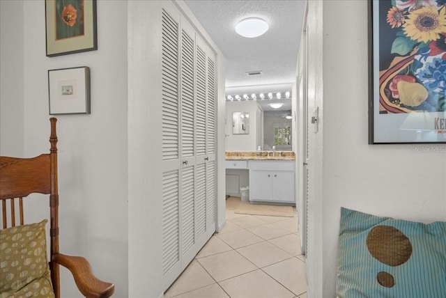 corridor with light tile patterned floors, a sink, visible vents, and a textured ceiling