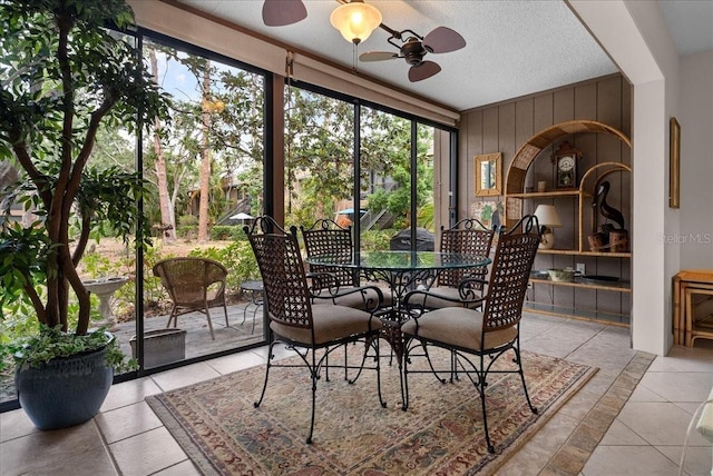 dining room with a ceiling fan, wood walls, light tile patterned floors, and a textured ceiling