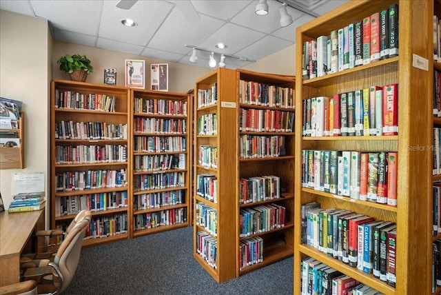 living area with a paneled ceiling, bookshelves, and carpet