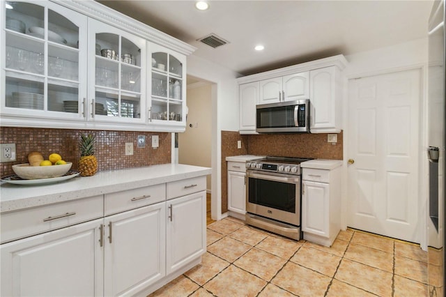 kitchen featuring white cabinets, appliances with stainless steel finishes, decorative backsplash, visible vents, and glass insert cabinets