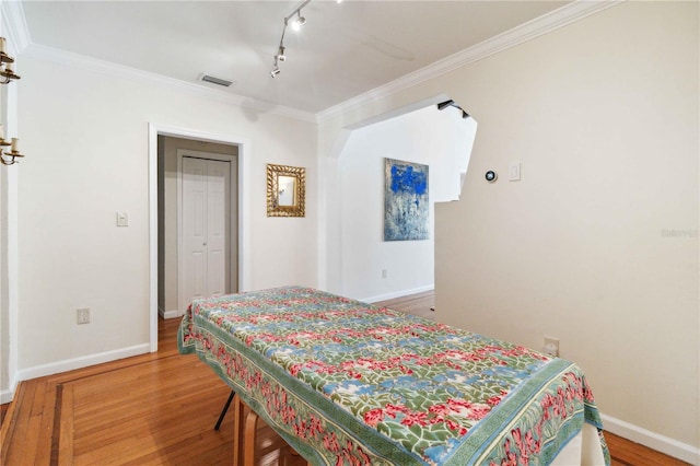 bedroom featuring track lighting, baseboards, wood finished floors, visible vents, and ornamental molding