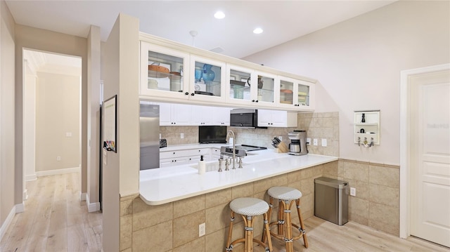 kitchen featuring stainless steel appliances, glass insert cabinets, light wood-style flooring, and a breakfast bar area