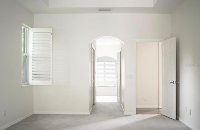 empty room featuring carpet flooring, arched walkways, baseboards, and plenty of natural light