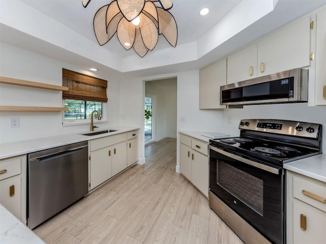 245 Woodingham Trl, Venice, FL 34292 - kitchen with stainless steel appliances, a sink, a raised ceiling, light countertops, and light wood-style flooring