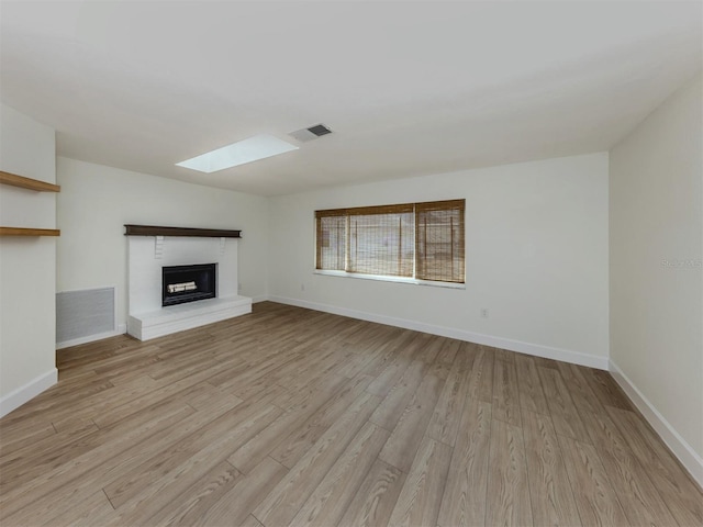 245 Woodingham Trl, Venice, FL 34292 - unfurnished living room with a skylight, light wood-type flooring, a brick fireplace, and baseboards