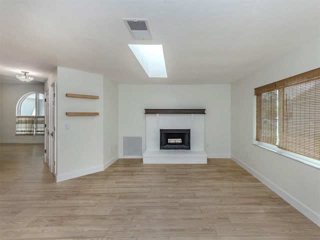 245 Woodingham Trl, Venice, FL 34292 - unfurnished living room with a fireplace with raised hearth, light wood-style floors, baseboards, and a skylight