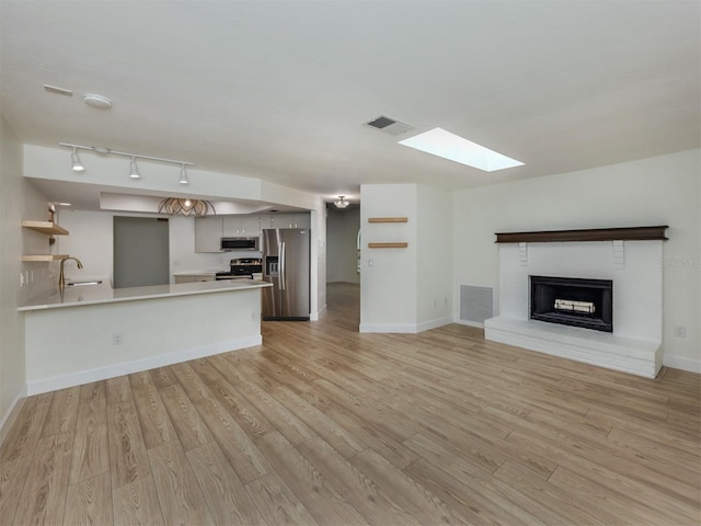 245 Woodingham Trl, Venice, FL 34292 - unfurnished living room featuring a skylight, a sink, light wood-type flooring, and a brick fireplace