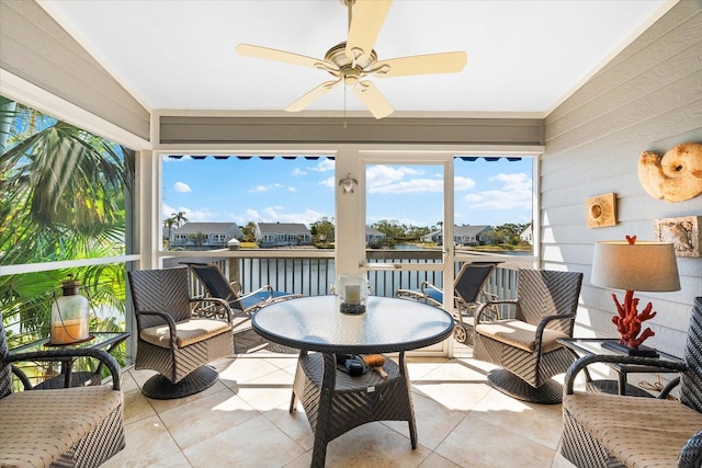 sunroom / solarium featuring tile patterned flooring, a ceiling fan, and a water view