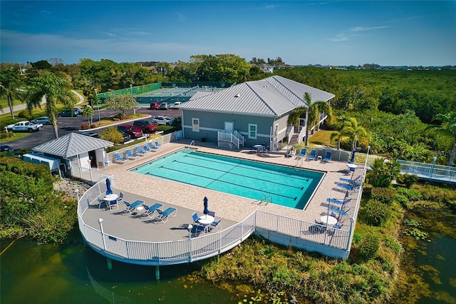 community pool with a patio, a water view, fence, and stairway
