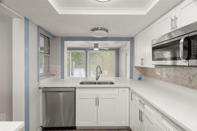 kitchen with a sink, backsplash, light countertops, white cabinets, and appliances with stainless steel finishes