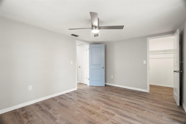 unfurnished bedroom featuring a closet, visible vents, light wood-style flooring, a spacious closet, and baseboards