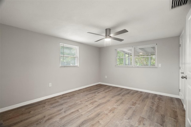 empty room featuring plenty of natural light, visible vents, wood finished floors, and baseboards