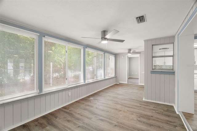 unfurnished sunroom with a ceiling fan, visible vents, and wood finished floors