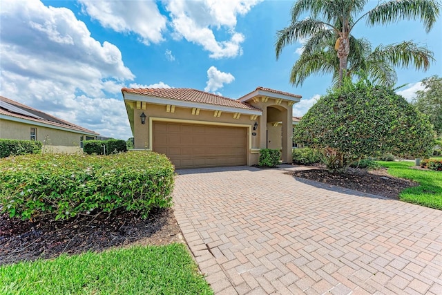 mediterranean / spanish-style home featuring stucco siding, a tiled roof, decorative driveway, and an attached garage