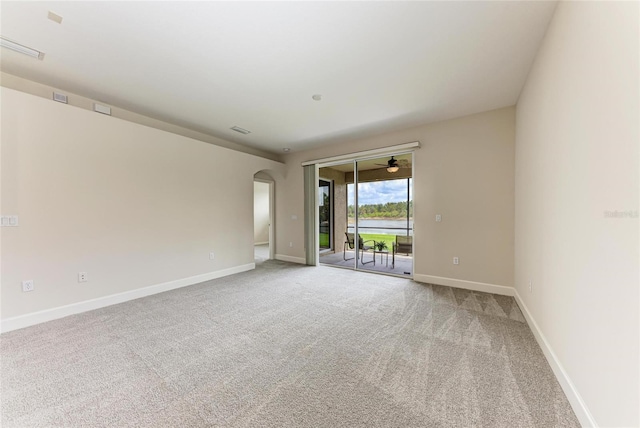 empty room featuring arched walkways, light carpet, ceiling fan, and baseboards