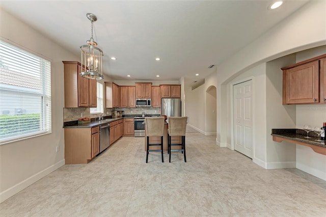 kitchen featuring stainless steel appliances, a sink, a breakfast bar, arched walkways, and decorative backsplash