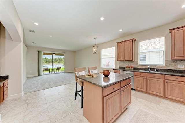 kitchen featuring dishwasher, a sink, light colored carpet, a kitchen island, and baseboards