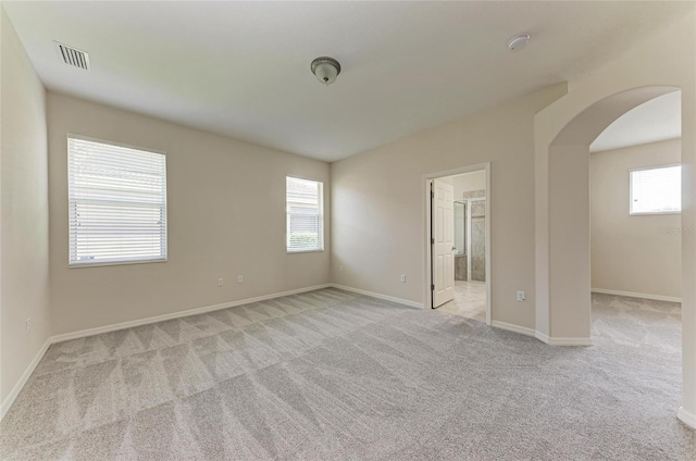 empty room with arched walkways, carpet floors, and healthy amount of natural light