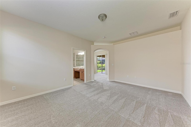 empty room with arched walkways, light colored carpet, and baseboards