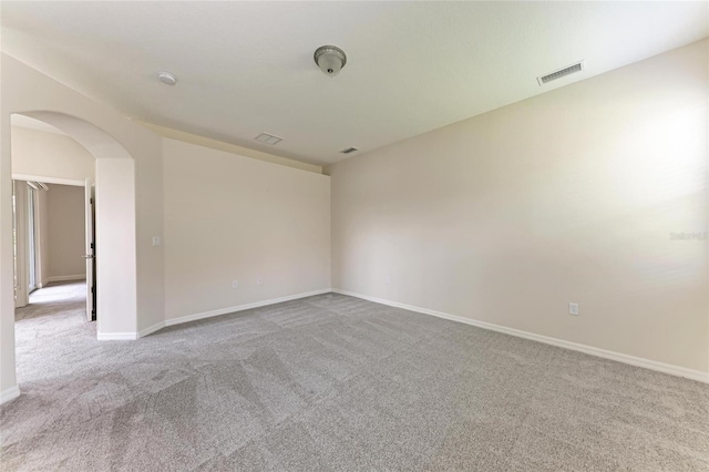 empty room featuring carpet, arched walkways, and baseboards