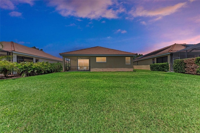 back of property at dusk with a tiled roof, stucco siding, and a yard