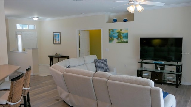 living area with ornamental molding, wood finished floors, ceiling fan, and baseboards