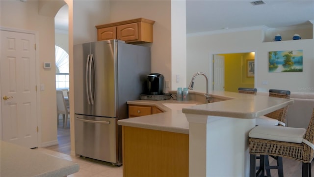 kitchen featuring freestanding refrigerator, a sink, a breakfast bar area, arched walkways, and ornamental molding
