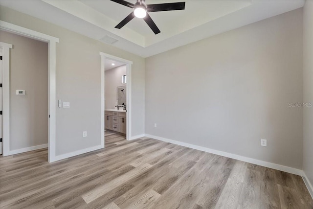 18274 Grace Ave, Port Charlotte, FL 33948 - unfurnished bedroom featuring light wood finished floors, a tray ceiling, ensuite bathroom, and ceiling fan