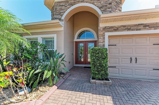 entrance to property featuring french doors, stucco siding, stone siding, and a garage