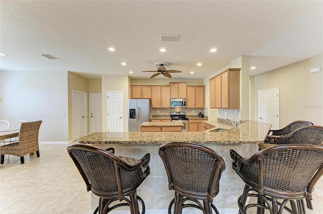 kitchen with appliances with stainless steel finishes, a sink, recessed lighting, light stone countertops, and a peninsula