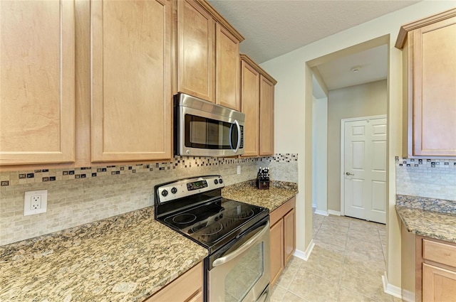 kitchen featuring stainless steel appliances, decorative backsplash, light stone counters, baseboards, and light tile patterned floors